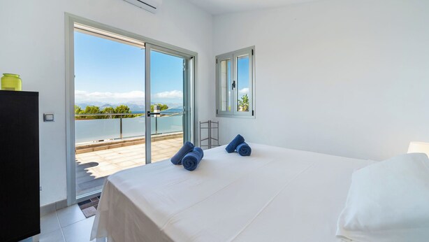 A bedroom with a large bed, a view of the sea, and a sliding glass door leading to an outdoor area. - Amanecer by Interhome (Alcúdia)