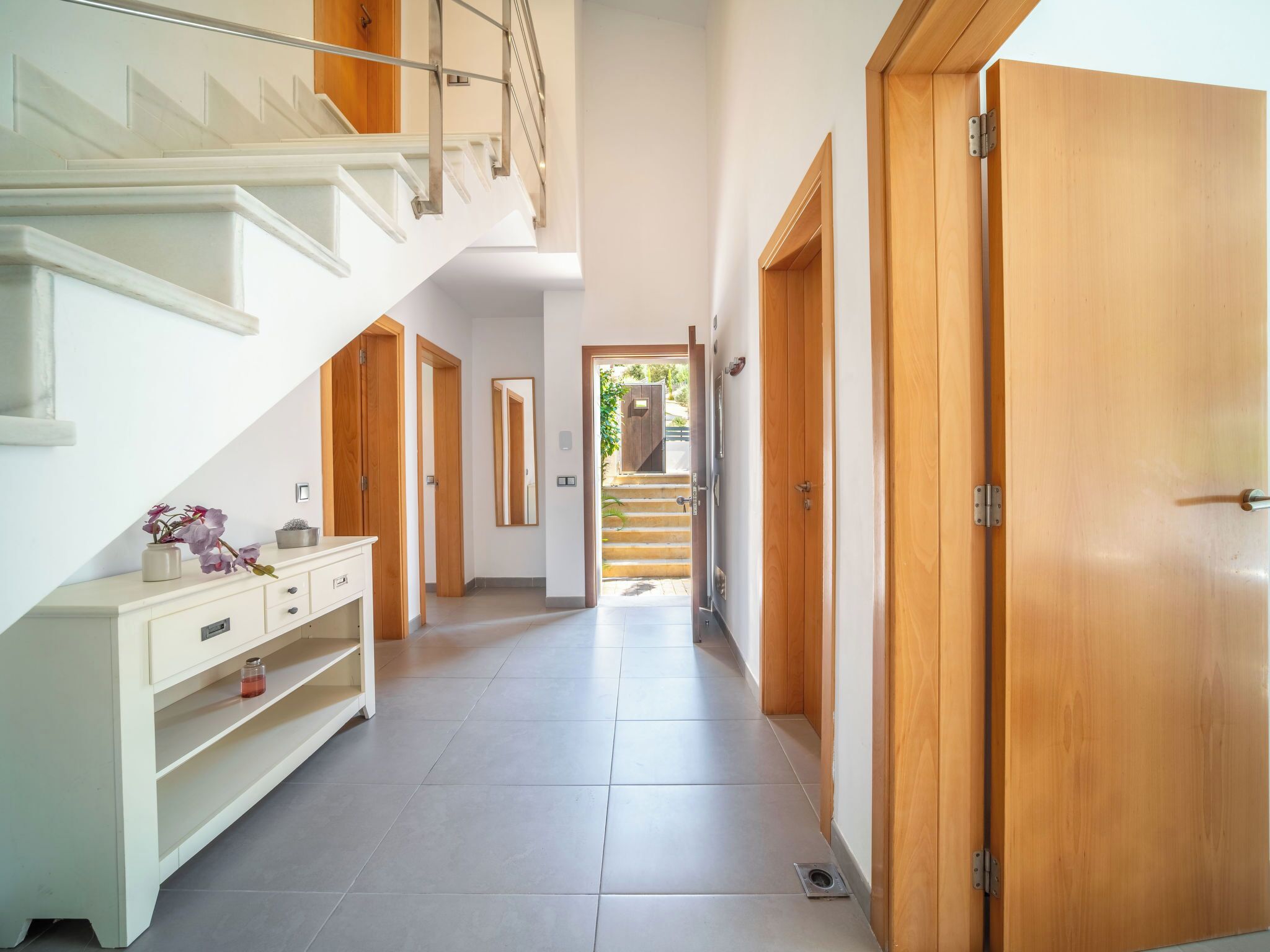 Ein moderner Flur mit Treppe, Holztüren und einem weißen Konsolentisch mit Dekorationen.