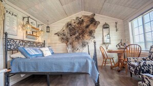 Una habitación con cama, una mesa de comedor, sillas, un gran cuero de animal colgado en la pared y un ventilador de techo.