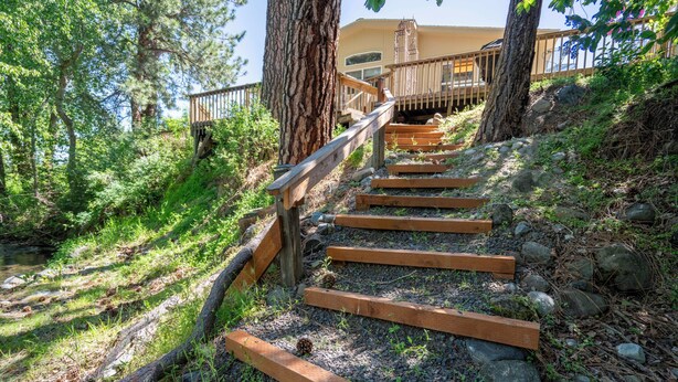 Una escalera de madera que lleva a un edificio con balcón, rodeado de árboles y un arroyo.