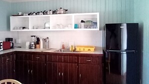 A kitchen with wooden cabinets, a black refrigerator, and white upper cabinets with dishes and kitchenware. - "Most Convenient Location For Your Vacation" (Eleuthera)
