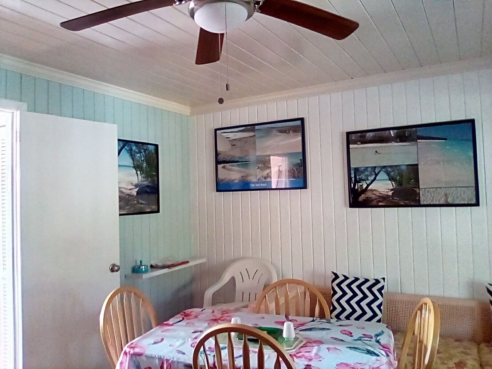 Un comedor con una mesa cubierta por un mantel floral, rodeada de sillas de madera. Encima de la mesa, hay tres cuadros en la pared.
