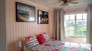 A bedroom with a bed, a ceiling fan, a window with curtains, and two framed pictures on the wall. - "Most Convenient Location For Your Vacation" (Eleuthera)