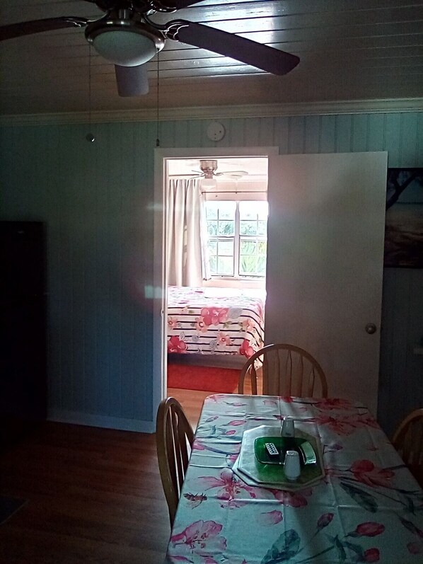 A room with a dining table, chairs, a ceiling fan, and a window with curtains.