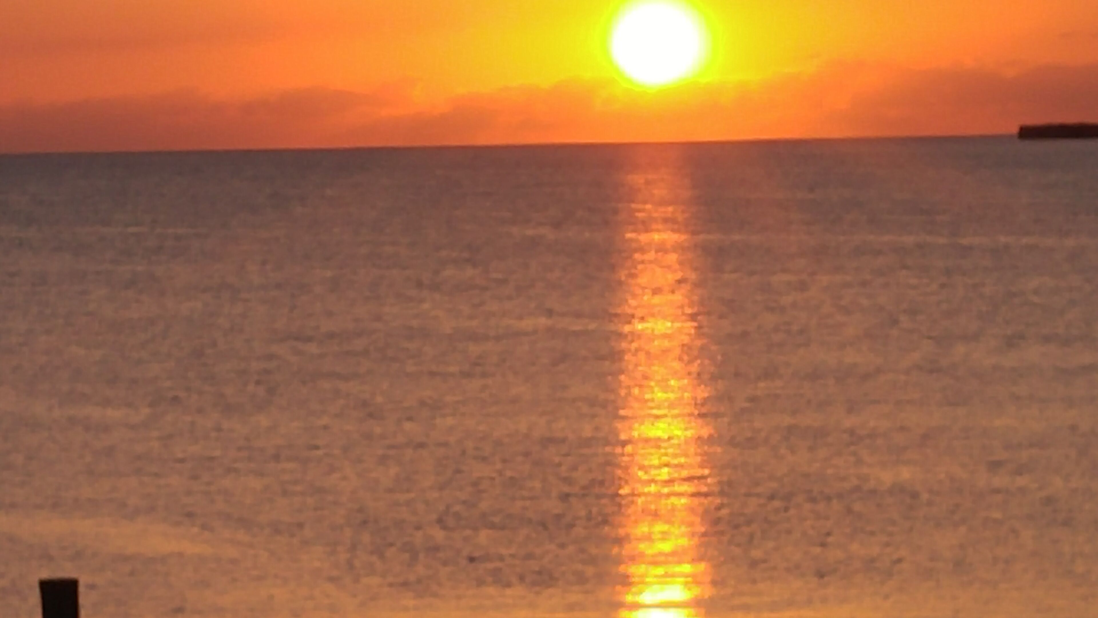 Un coucher de soleil sur une mer calme, avec un horizon dégagé.