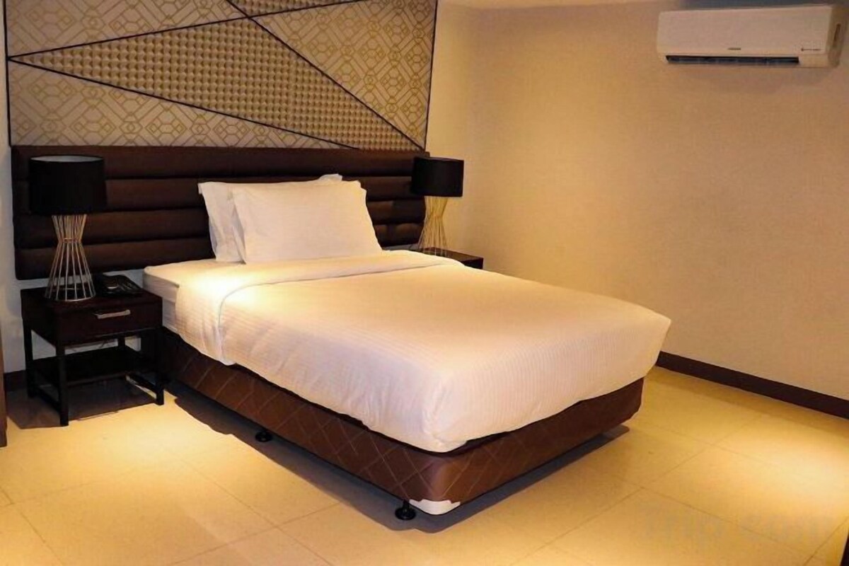 A neatly made bed with white linens and a wooden headboard in a hotel room.
