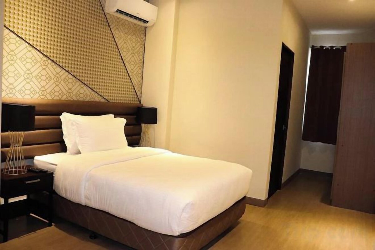 A hotel room with a large bed, a bedside table, a wall-mounted air conditioner, and a patterned wall design.