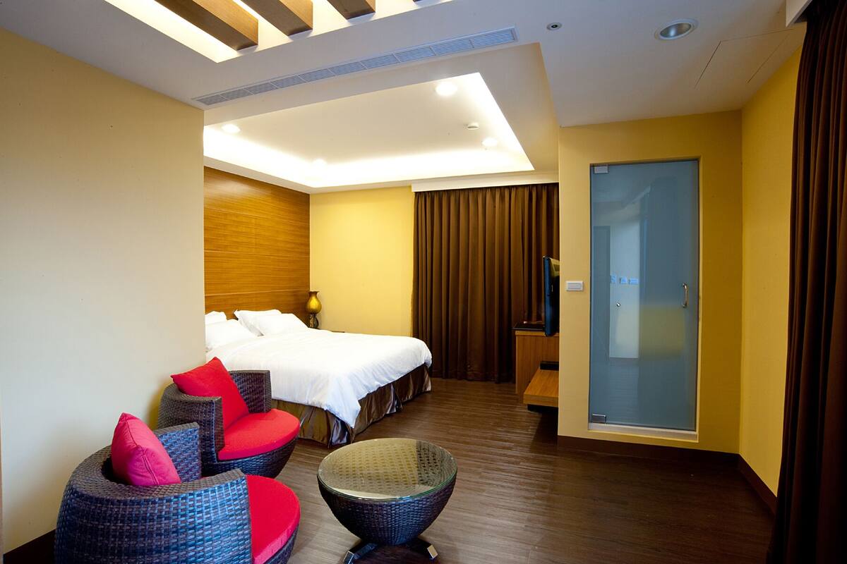A hotel room with a bed, a TV, a seating area with chairs, and a glass door.