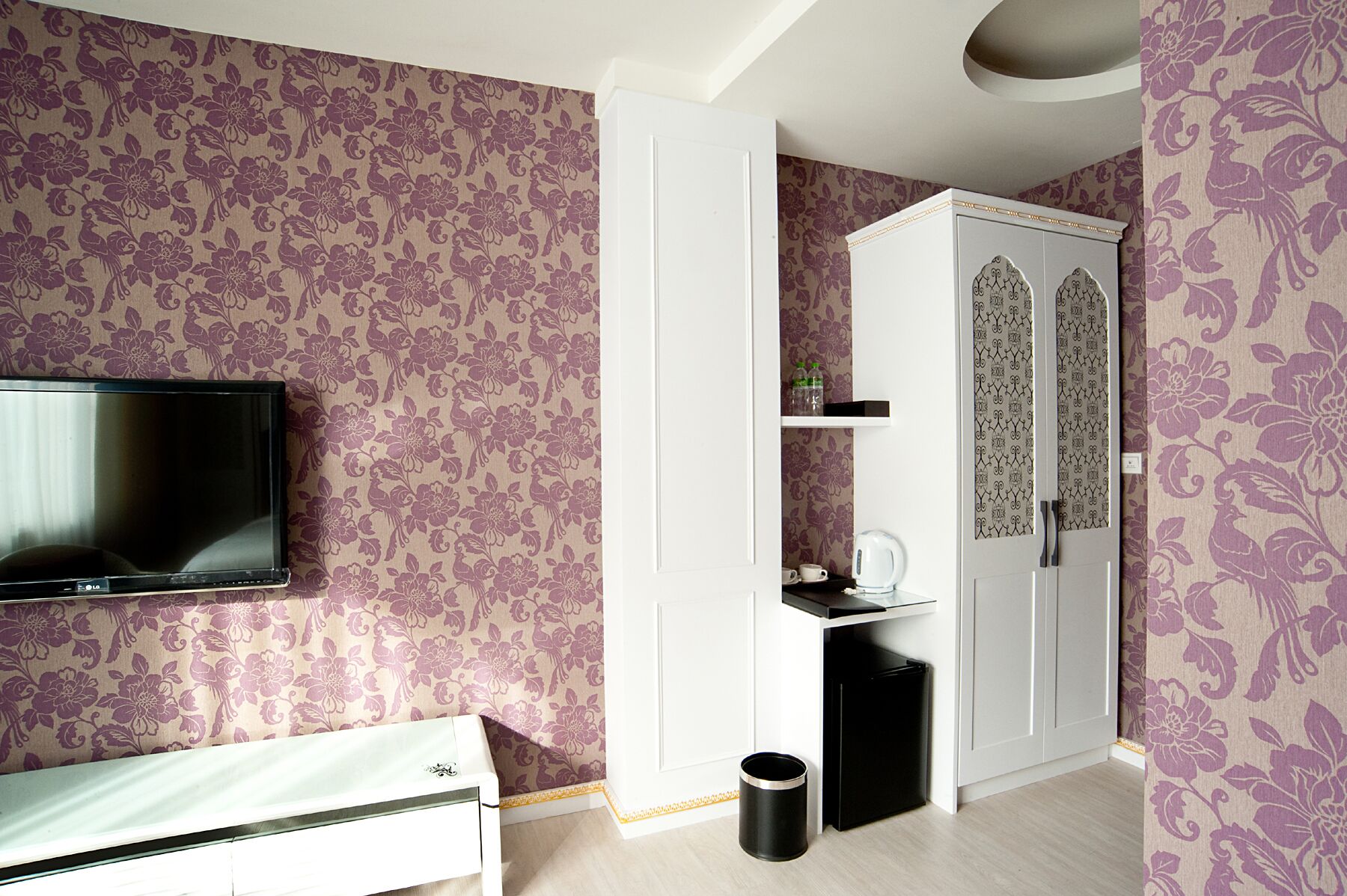 Ein Zimmer mit blumigem Wandpapier, einem Fernseher, einem Kleiderschrank und einer Mülltonne.
