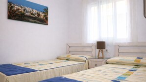 A bedroom with two single beds, a bedside table with a lamp, and a window with sheer curtains.