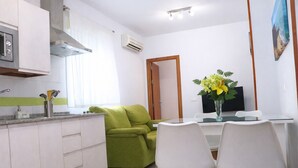 A compact kitchen with a built-in oven, a dining area with a table and chairs, and a green sofa.