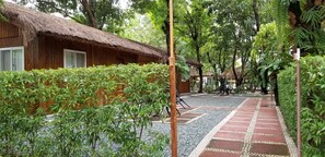 A wooden building with a thatched roof, surrounded by lush greenery and a gravel pathway. - Buenavista Family Inn (Tagudin)