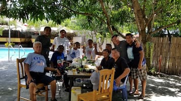 A group of people gathered around a table with drinks, outdoors near a pool.