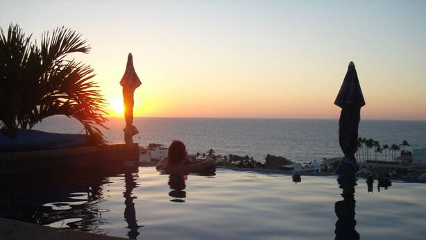 A serene pool area with a sunset view, palm trees, and a calm sea. - lovely suite getaway (Puerto Vallarta)