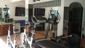 A home gym with exercise equipment including a stationary bike, elliptical, treadmill, and weights. - lovely suite getaway (Puerto Vallarta)