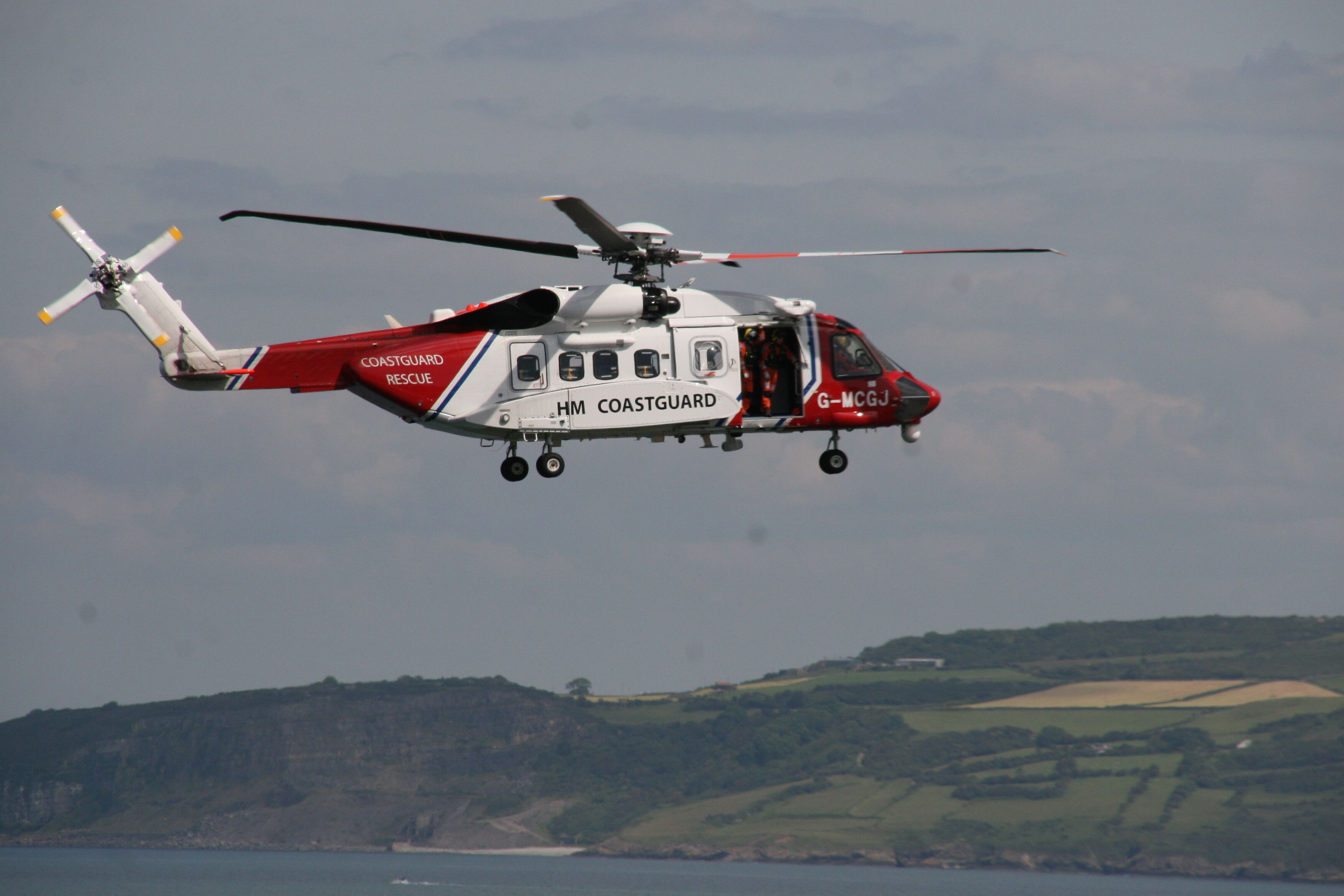 A Coastguard rescue helicopter in flight with a clear view of the landscape below.