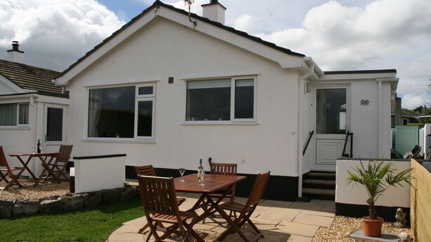 A white mobile home with a patio area, including a wooden table and chairs, a potted plant, and a small statue. - Penmon View, Moelfre, Anglesey. With sea and mountain views. (Moelfre)