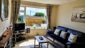 A living room with a black leather sofa, a wooden coffee table, a TV on a stand, and a window with curtains. - Penmon View, Moelfre, Anglesey. With sea and mountain views. (Moelfre)
