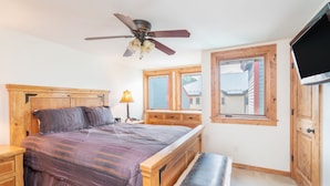 A bedroom with a wooden bed, a ceiling fan, a window with a view, and a TV on the wall. - Beautifully Remodeled - Steps to Lift 7 and River Trail with Mountain Views (Telluride)