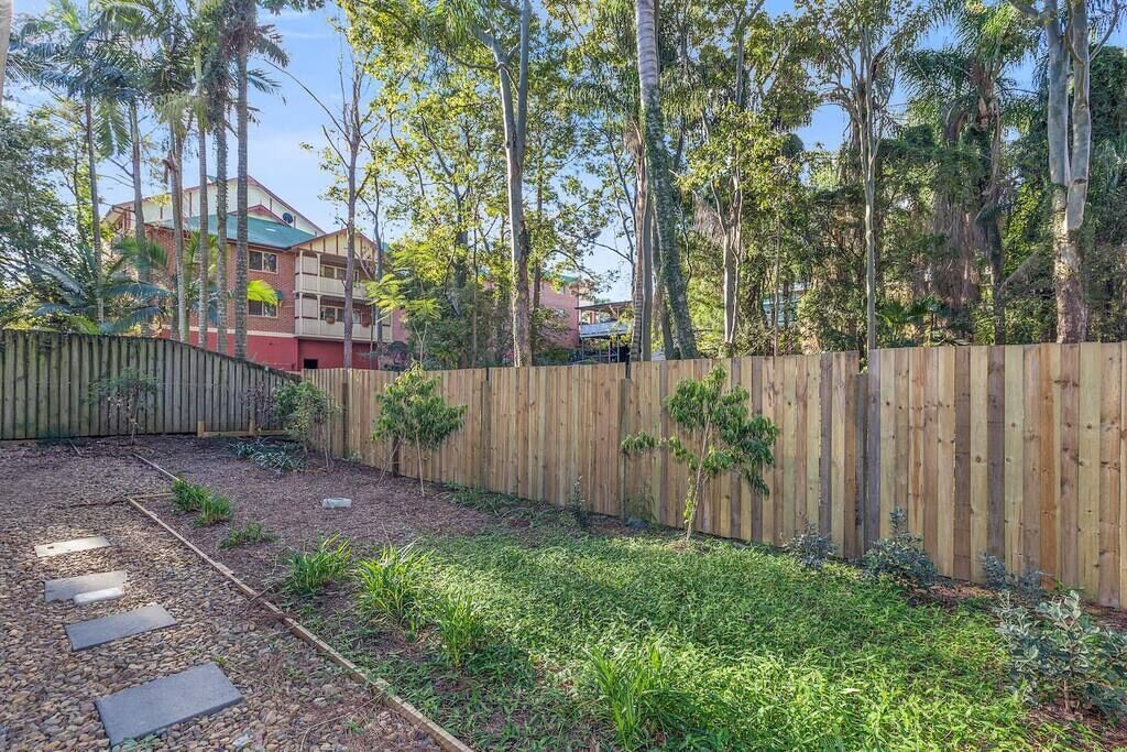 A backyard with a wooden fence, a paved pathway, and a variety of plants.