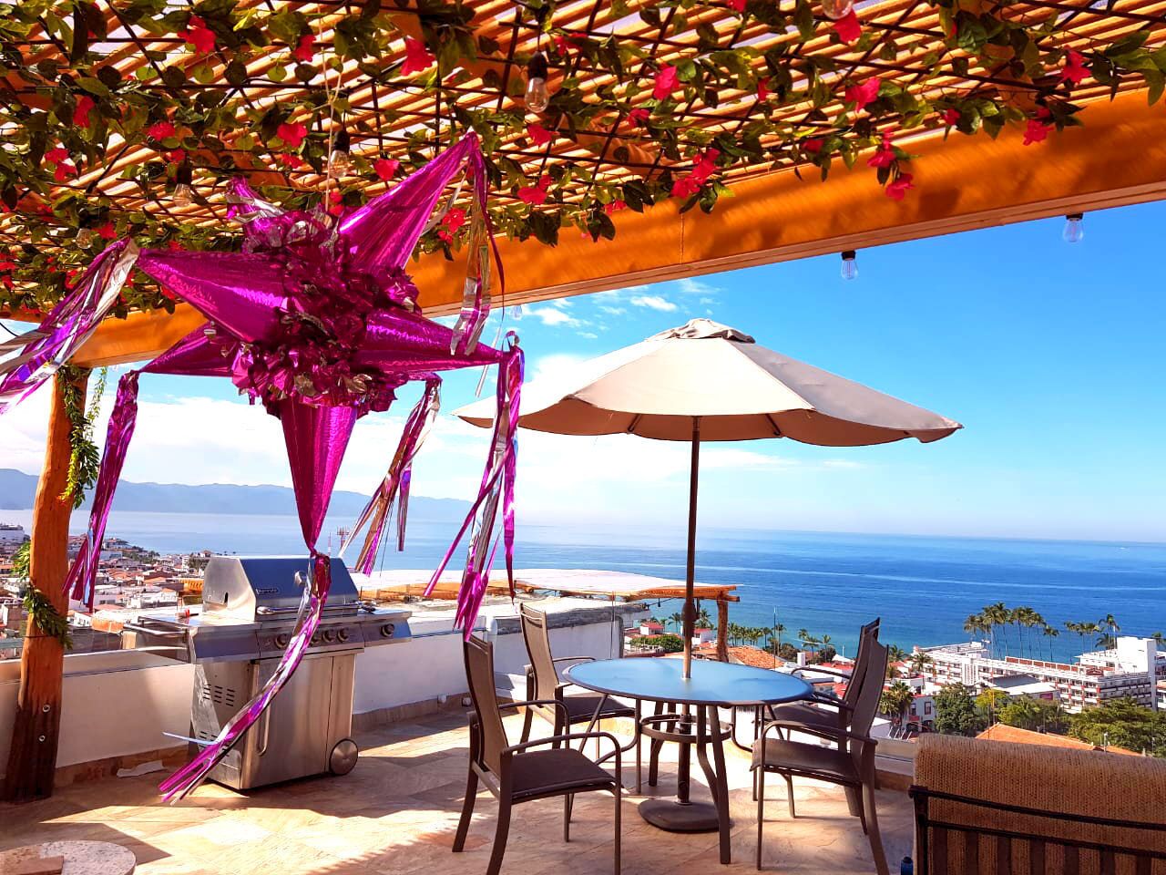 An outdoor patio with a grill, dining table, chairs, and a view of the ocean.