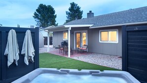 Ein Garten mit Whirlpool, Grill und einer Terrasse mit Stühlen und Tisch.