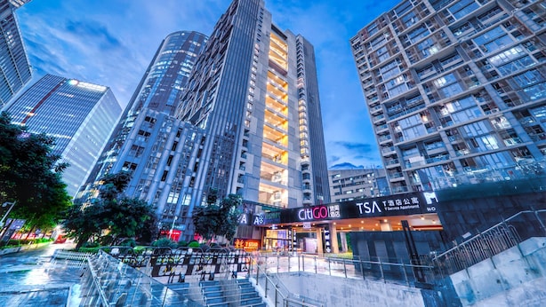 Um edifício alto com vários andares, uma entrada destacada com sinalização e uma escadaria que leva à entrada.