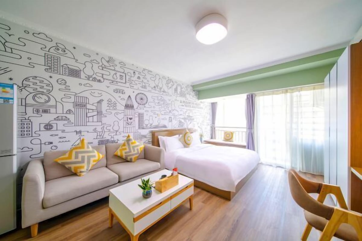 A hotel room with a bed, a sofa, a coffee table, and a wall with cityscape drawings.