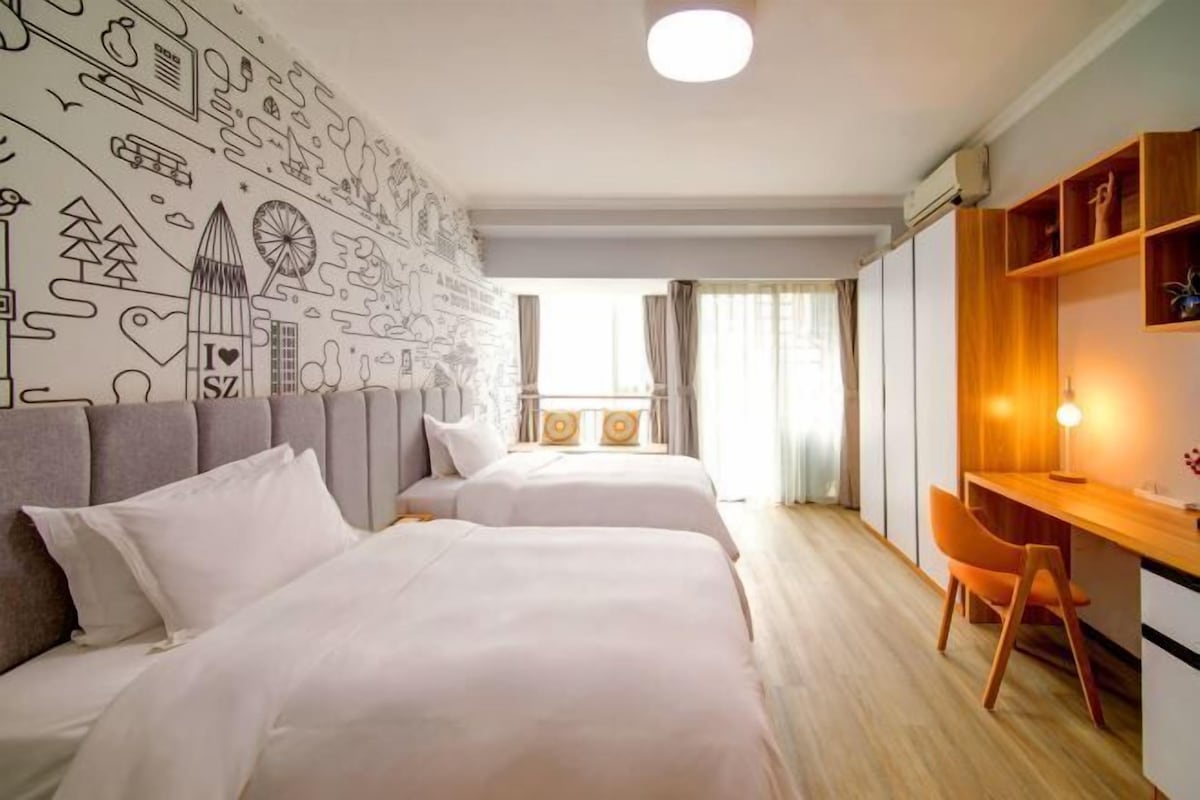 A hotel room with two beds, a desk, and a view of the city.