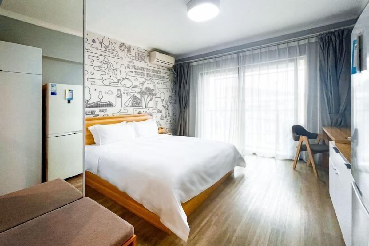 A hotel room with a bed, a desk, a chair, a wardrobe, and a window with curtains.