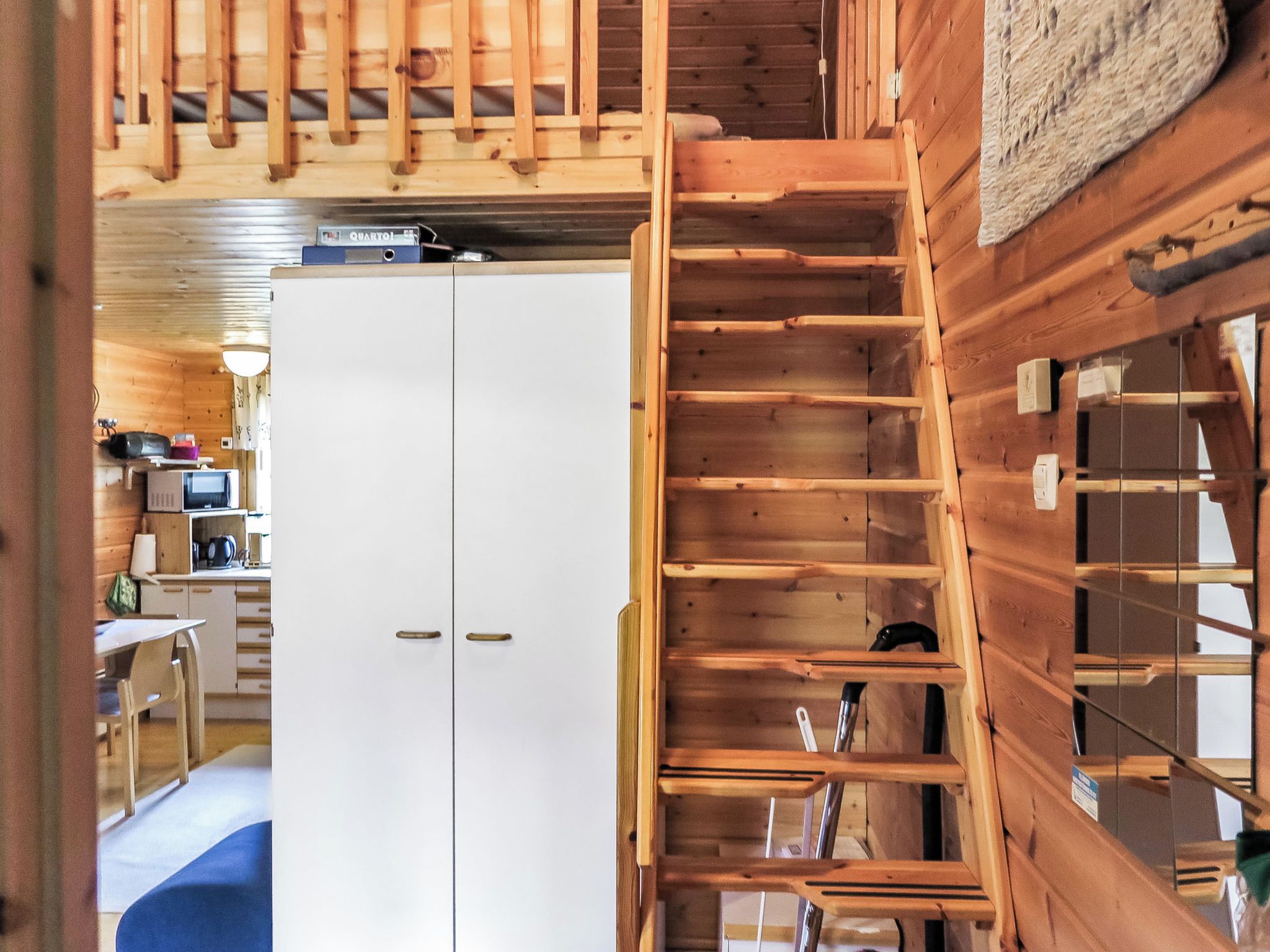 Een houten interieur met een witte kast, een houten trap en een keuken met een magnetron.