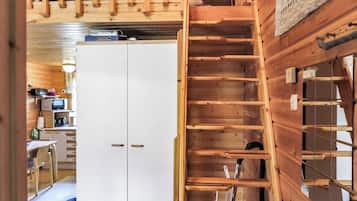 A wooden interior with a white wardrobe, a wooden staircase, and a kitchen area with a microwave.