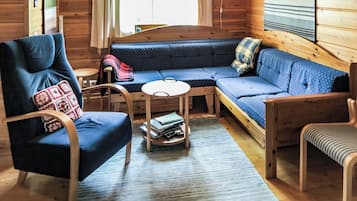 A cozy cabin interior with a blue sofa, a wooden chair, a small round table, and a bookshelf.