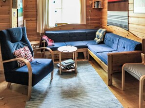 A cozy cabin interior with a blue sofa, a wooden chair, a small round table, and a bookshelf.