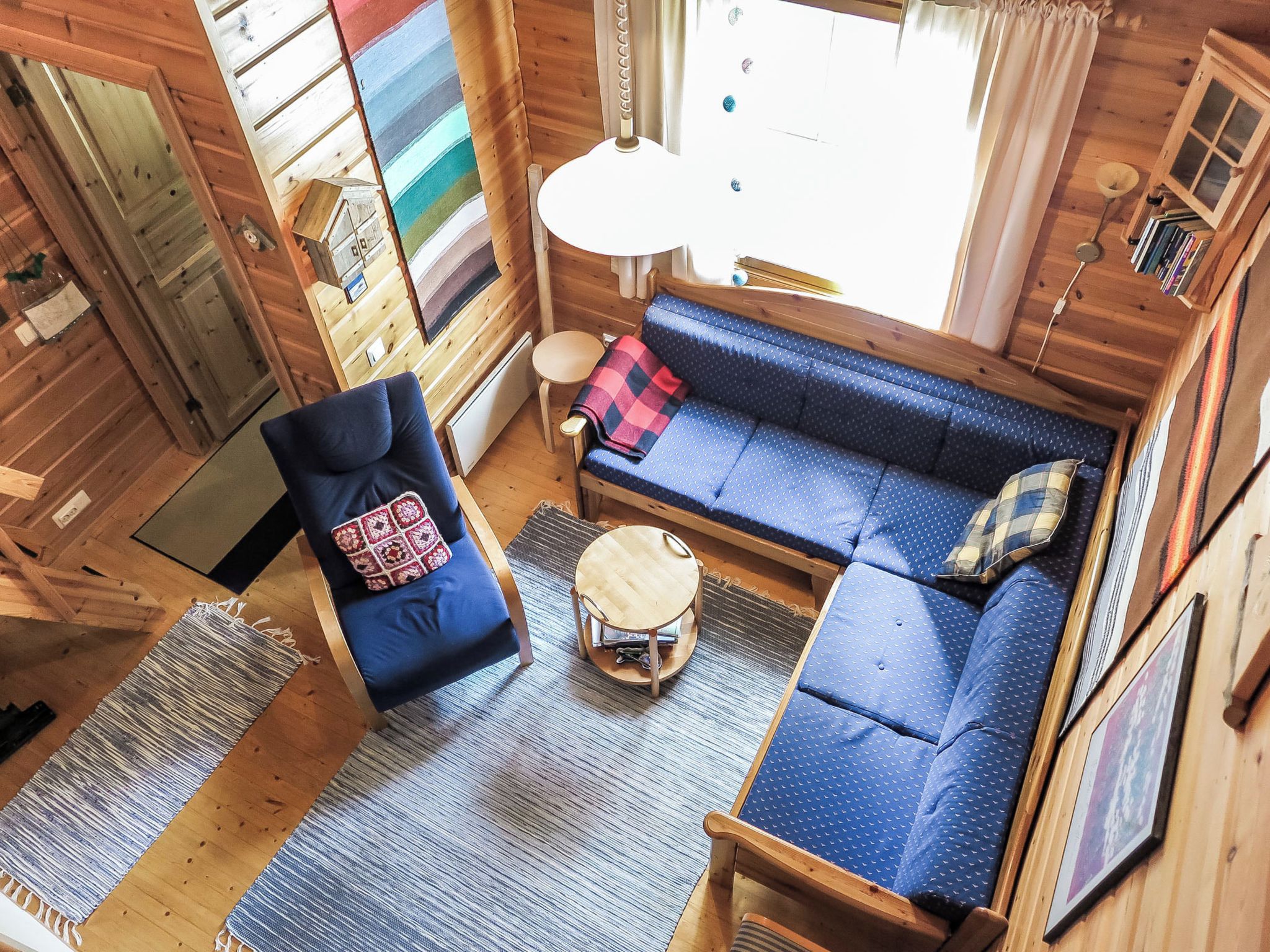 A cozy cabin interior with a blue sofa, a chair, a small round table, and a window with curtains.
