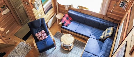 Ein gemütliches Blockhausschlafzimmer mit einem blauen Sofa, einem Sessel, einem kleinen runden Tisch und einem Fenster mit Vorhängen.