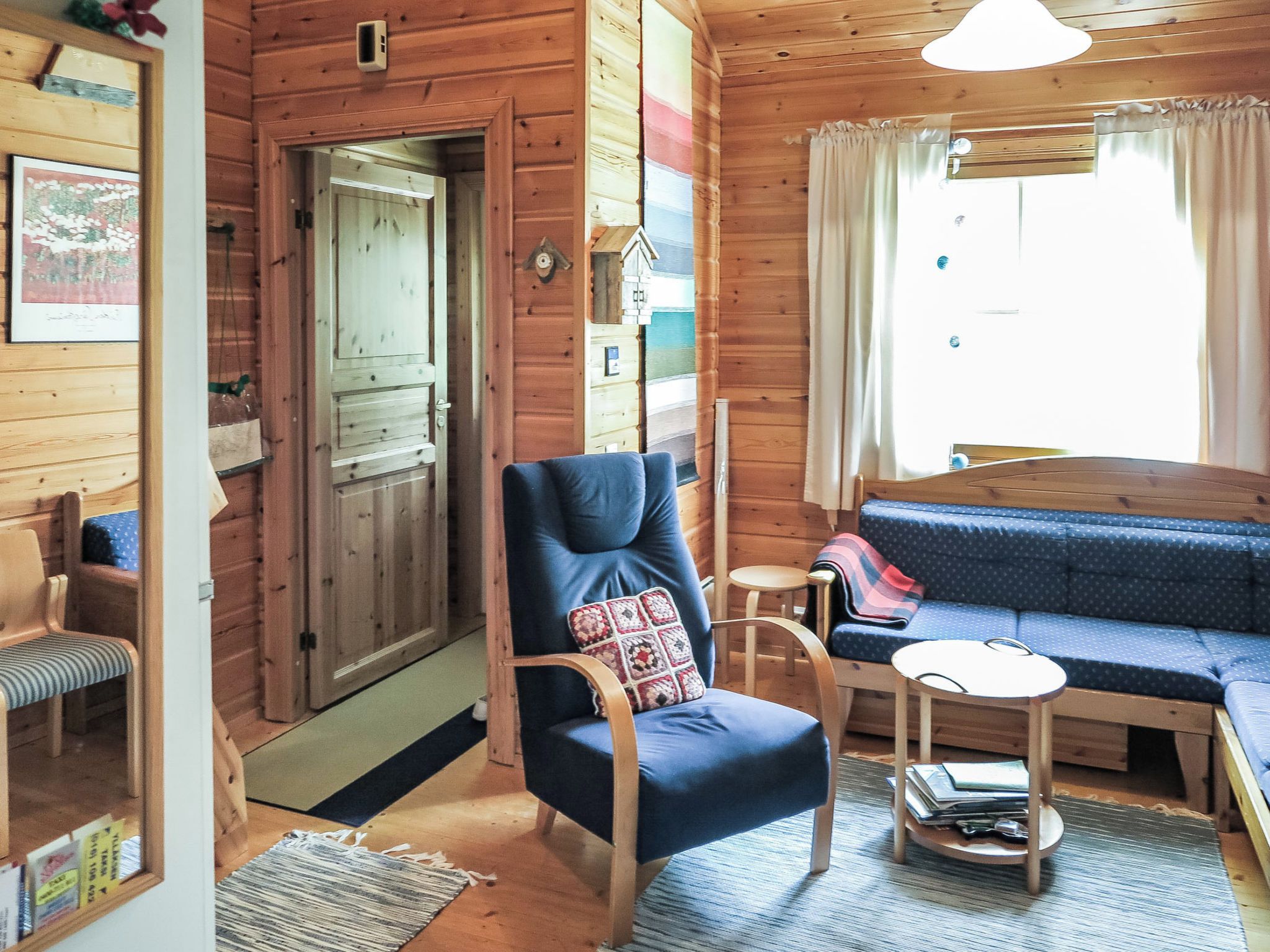 A cozy cabin interior with a wooden door, a blue armchair, a small table, and a blue sofa.