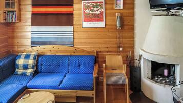 L’intérieur d’un chalet accueillant, avec un canapé en bois, une petite table, une chaise, une cheminée et un téléviseur.