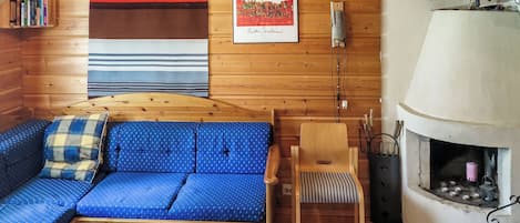 A cozy cabin interior with a wooden sofa, a small table, a chair, a fireplace, and a television.