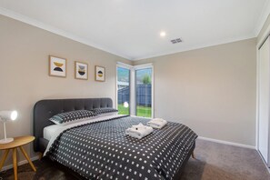 A bedroom with a large bed, a bedside table, a lamp, and a view of the outdoors. - Apollo Grand (Apollo Bay)
