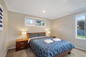 A bedroom with a bed, two bedside tables, a window, and a view of the outside.