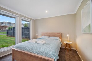 A bedroom with a bed, two bedside lamps, a window, and a view of the outside.