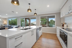 A modern kitchen with a large island, built-in appliances, and large windows offering views of the outdoors.