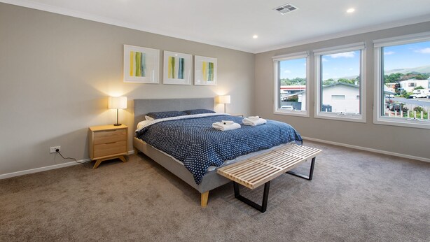 A bedroom with a bed, bedside lamps, a bench, and a large window with a view.