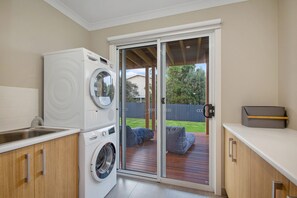 A compact kitchen with a built-in washer and dryer, a sink, and a sliding glass door leading to an outdoor deck. - Apollo Grand (Apollo Bay)
