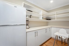 A modern kitchen with white cabinetry, a built-in blender, and a white high chair.