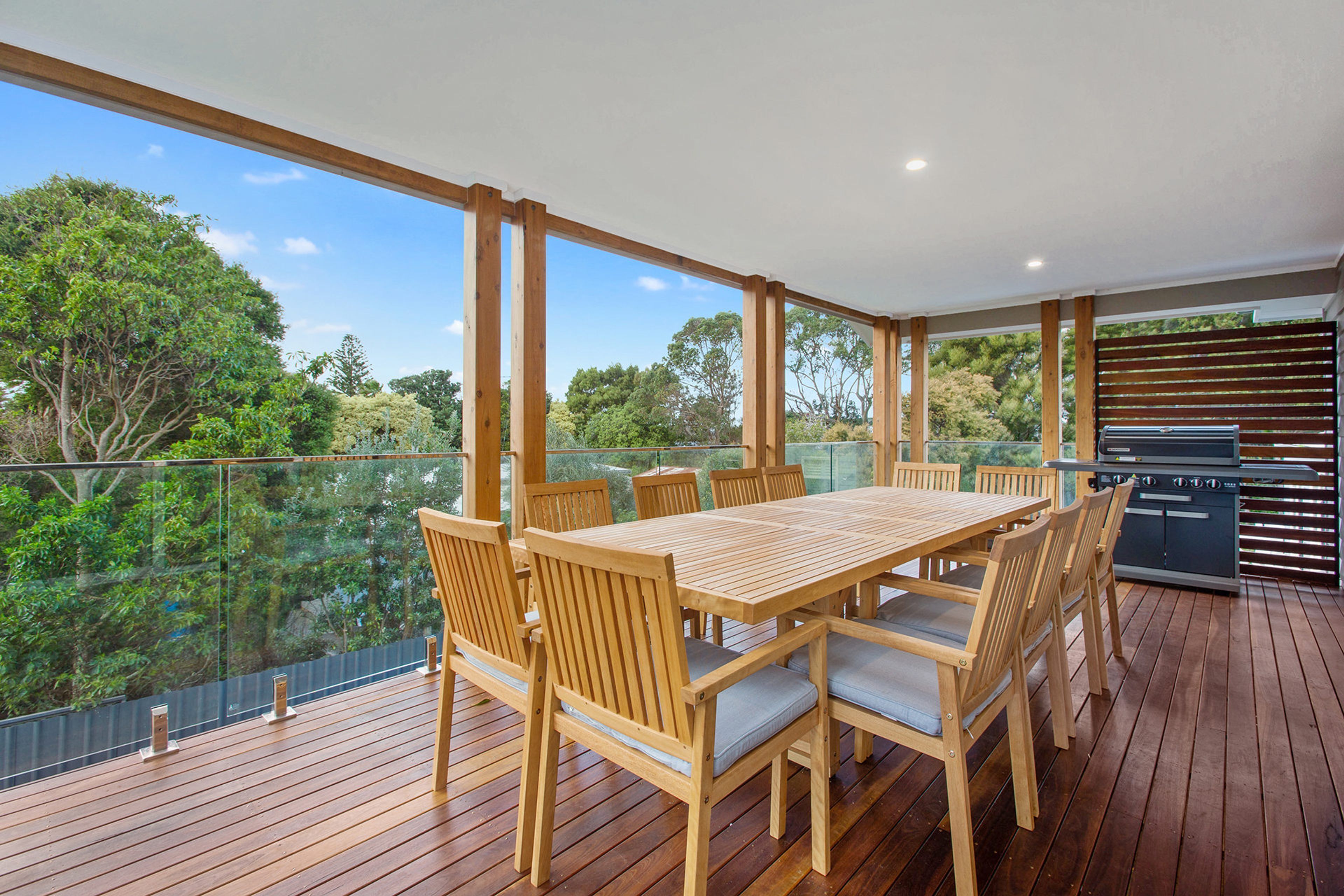 A wooden deck with a dining table and chairs, overlooking a body of water and trees.