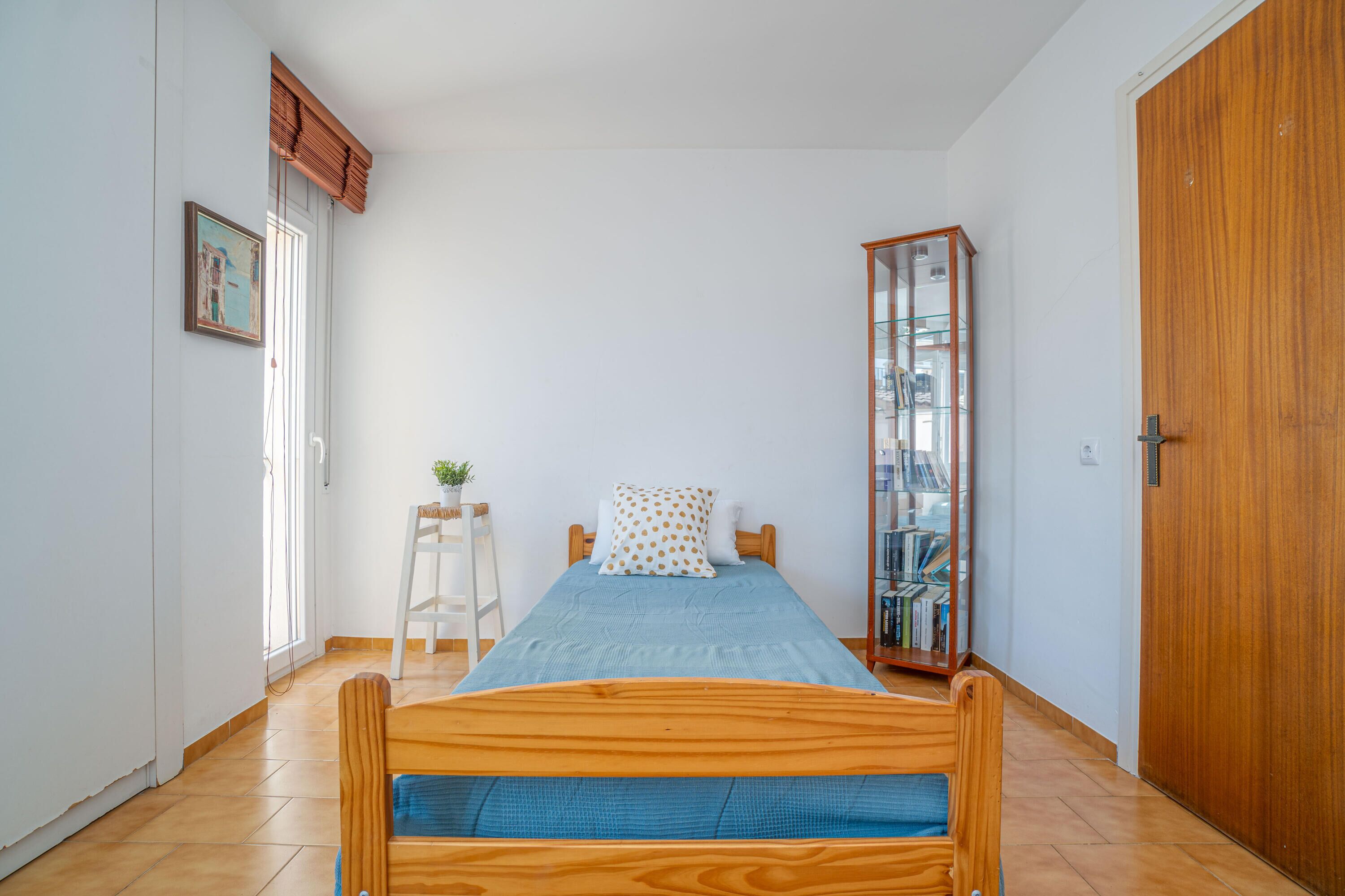 Une chambre à coucher avec un lit en bois, une table de chevet ornée d’une plante, une armoire et une bibliothèque.