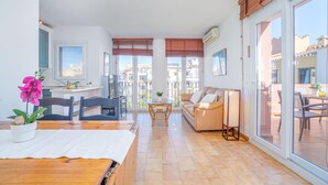 Un vaste espace de vie comprenant un canapé, une table à manger et des chaises, de grandes fenêtres équipées de stores et une vue sur les bâtiments environnants.