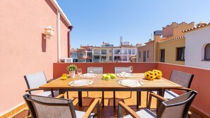 Une terrasse avec une table en bois, dressée pour le repas, entourée de chaises, et offrant une vue sur le paysage urbain.